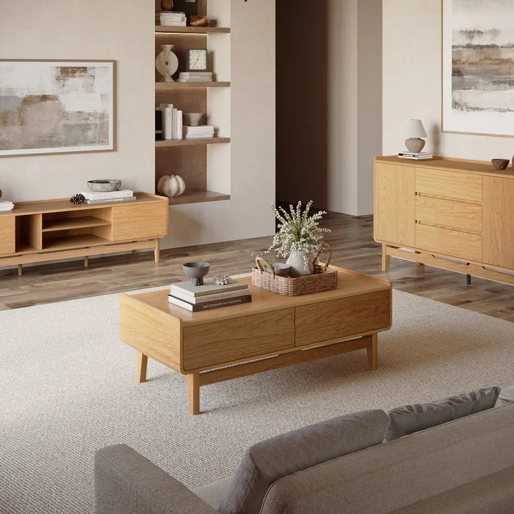 A modern living room with light wood furniture, including a coffee table, sideboard, and TV stand, neutral wall art, and decorative items on shelves.