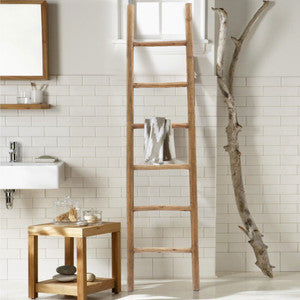 light wood tone blanket ladder in a modern bathroom on the side of a wood end table leaning on a wall covered with white ceramic tiles