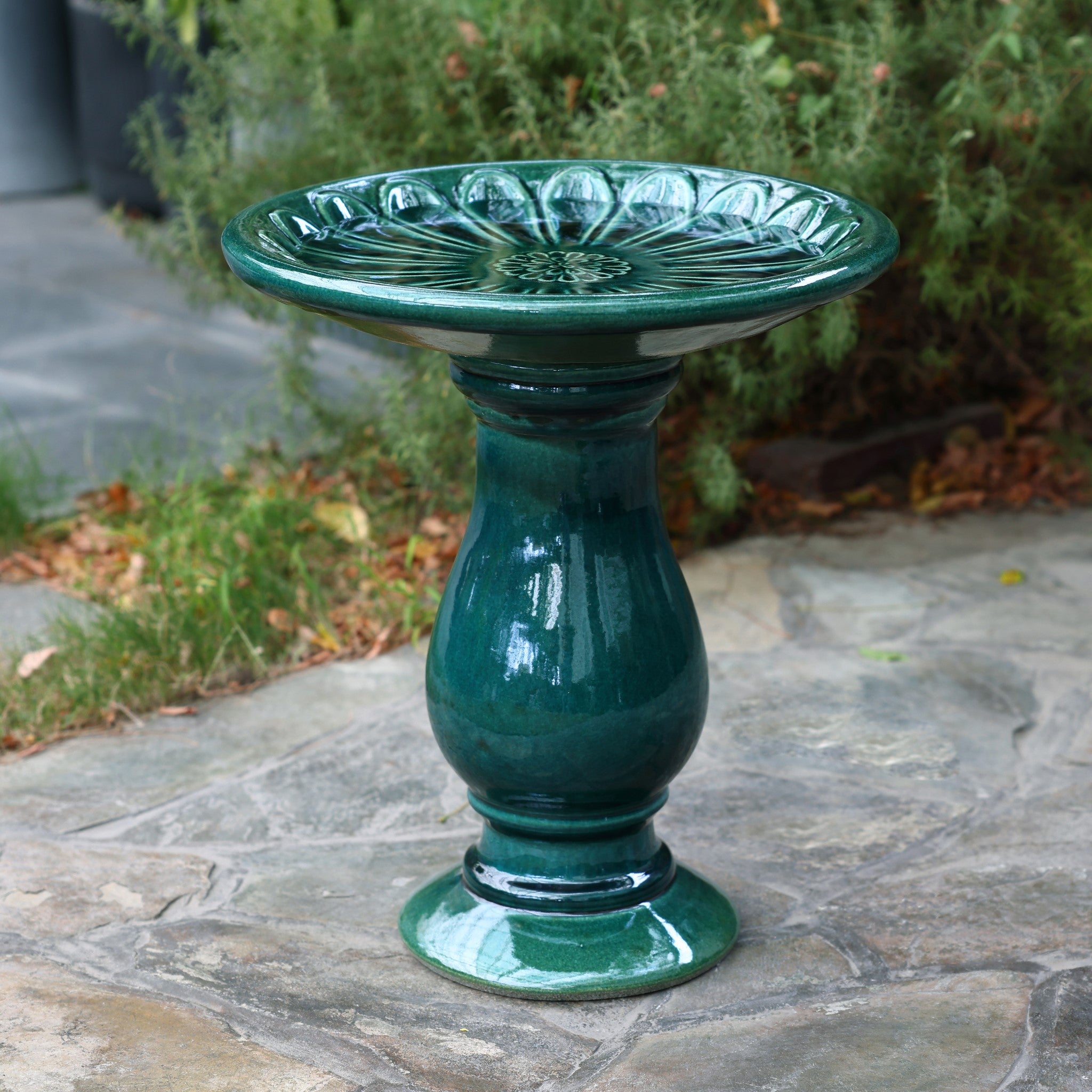 A charming green ceramic birdbath with a lovely flower pattern graces the stone patio, creating a serene focal point in the outdoor space surrounded by lush greenery.