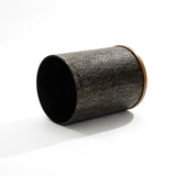 A textured, cylindrical container with a brown rim lies on its side against a white background, reminiscent of the elegant fusion found in a black and gold table.