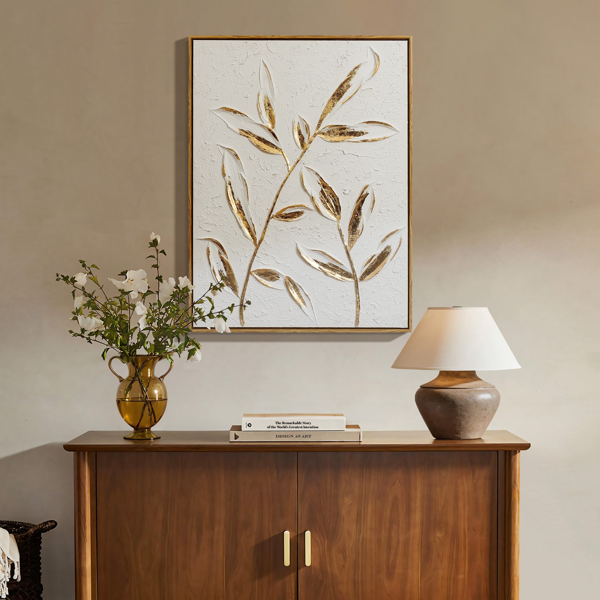 Wooden sideboard with a potted plant, books, and a lamp. Above, a modern wall decor piece showcasing an elegant gold leaf motif.