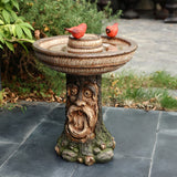 This outdoor decor centerpiece features an ornate birdbath with a carved wooden base resembling the face of a brown old man tree, topped with two small red bird figurines.