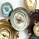 A collection of decorative ceramic plates in various metallic shades, including gold, turquoise, and brown, creates an abstract design as they overlap each other against a white background. Perfect as metal wall art or a unique wall decoration.