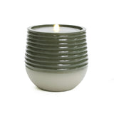 A lit candle in a ribbed design, two-toned ceramic holder with dark green and light gray colors adds an elegant touch, blending seamlessly with modern LED lights.