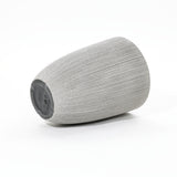 A gray, concrete-textured cylindrical speaker with a slanted top rests on its side against a white background.