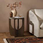 A small walnut veneer table with a vase, a decorative jug, and a glass near a beige sofa. The floor features a patterned rug.