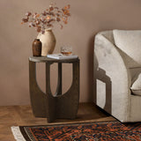 A small walnut veneer table with a vase, a decorative jug, and a glass near a beige sofa. The floor features a patterned rug.