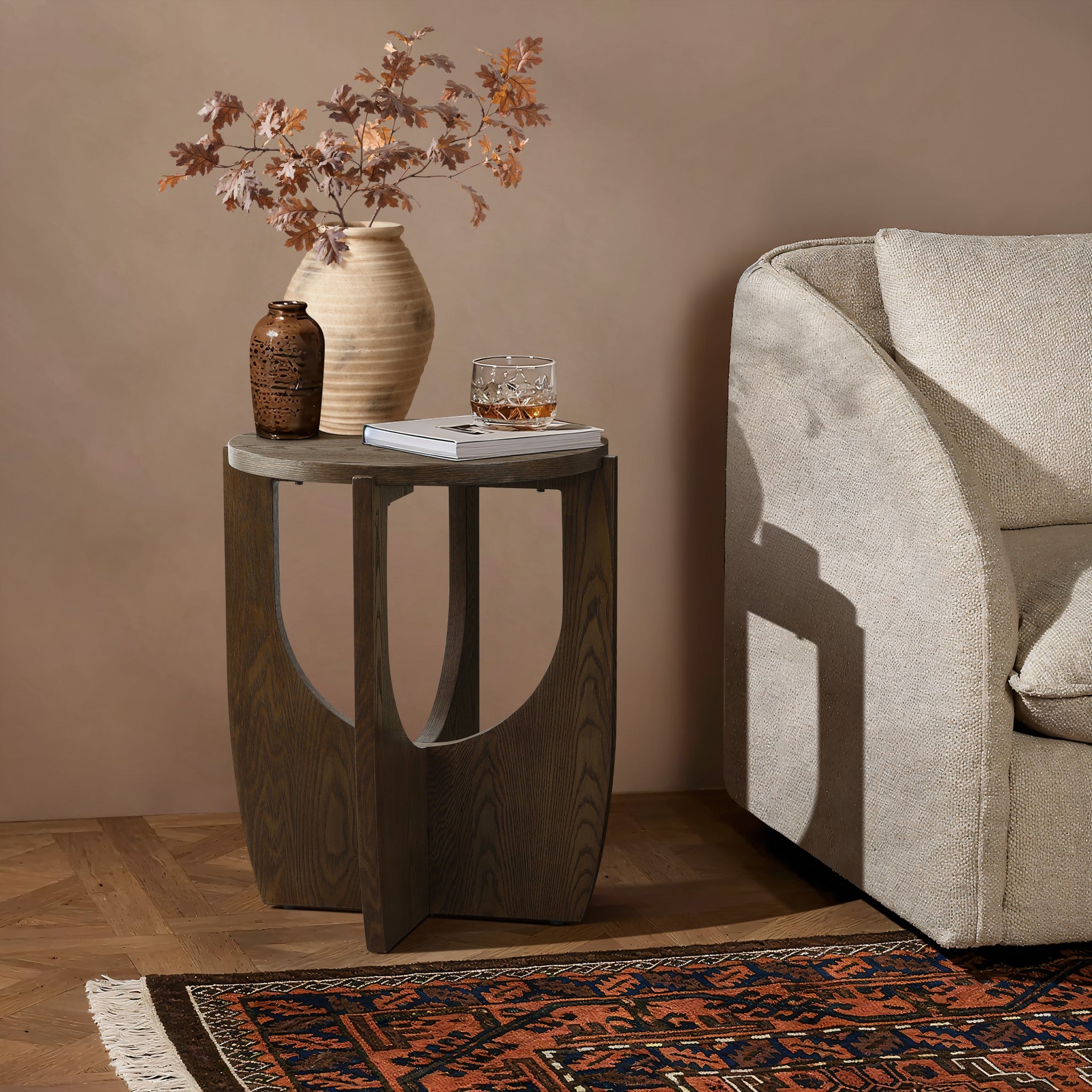 A small walnut veneer table with a vase, a decorative jug, and a glass near a beige sofa. The floor features a patterned rug.