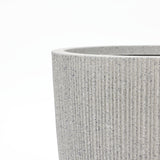 Close-up of a textured, gray cylindrical container with vertical grooves resembling striped planters on the surface, set against a plain white background.