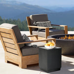 cement outdoor end table by the side of solid teak wood outdoor accent chair with grey cushions, in front of cement outdoor fire pit