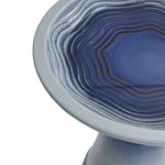 Close-up of a ceramic bird bath with concentric blue ripples in the center, resembling waves, set against a lighter outer edge.