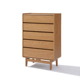 The LuxenHome Eric 5-drawer chest features a tall, minimalist design in an oak finish. This Mid-Century Modern piece stands on short legs, casting subtle shadows below.