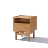 This Eric oak finish nightstand by LuxenHome showcases a smooth mid-century design with one drawer, an open shelf above, and short, tapered legs for a modern touch.