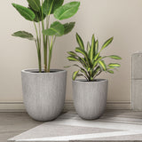 Two potted plants in gray textured planters are on a light-colored floor next to a rug and a sofa, adding a touch of home and garden elegance. The modern striped pattern on the wall complements the serene setting perfectly.