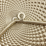 Close-up of a textured metallic pattern resembling a spiral, with a central metal rod and loop integrated into the design, evoking the charm of vintage metal wall decoration.