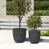 Two minimalist design planters in textured dark gray containers grace an outdoor patio near the steps.