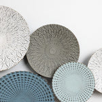 A collection of decorative ceramic plates with intricate patterns in shades of gray, white, and blue adds an artistic touch to your home decor when elegantly arranged on a white surface.
