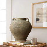 The LuxenHome rustic brown terracotta cauldron vase, 14.6 h, with two handles sits on a stack of books on a woven tray. A small gray cup is nearby, and a black-and-white tree artwork hangs behind as sunlight streams in, enhancing the natural elegance of the decor scene.