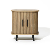 The Aria oak finish nightstand by LuxenHome offers a modern, mid-century vibe with its rounded design and slatted sliding door. It serves as a perfect bedside table featuring two black handles and sturdy short black legs on a plain white background.