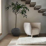 A modern interior features a neutral-toned armchair, a gray potted plant in a sleek modern planter, and floating stairs on a light wooden floor.