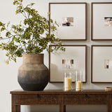 A rustic living room highlights a LuxenHome brown ombre terracotta round vase (13.2 h) with leafy branches on a wooden console. Two glass candles complement the setup, while four framed abstract art pieces on the wall complete the minimalist touch to the vintage look.