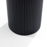 Close-up of a round, vertically ribbed, black side table with smooth, shadowed lighting on a white background, showcasing a modern aesthetic.