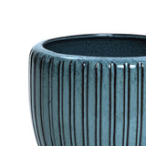 A close-up of a sea-green ceramic flowerpot highlights its vertical ridges and textured surface, beautifully capturing the rounded edge crafted from high-quality materials.