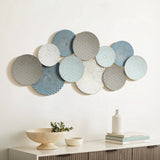 A vintage metal wall decoration, this abstract wall art showcases a series of overlapping circular metal discs in hues of blue, gray, and white with intricate patterns, elegantly mounted above a cabinet adorned with decorative items.