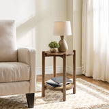 A wooden side table with a chestnut finish, adorned with a lamp, a small plant, and books, sits gracefully next to a cream-colored armchair in the sunlit room.