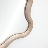 Close-up of a decorative wall mirror with a natural wooden frame, its curvy design beautifully highlighted against the white wall.