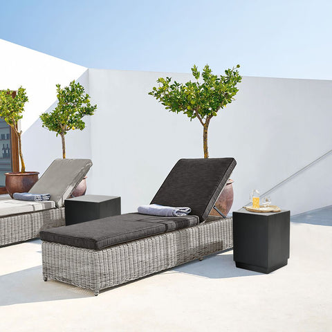 cement outdoor end table by the side of synthetic rattan woven outdoor lounge chairs in a backyard setup