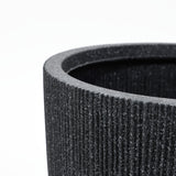 Close-up of a concrete-textured, cylindrical black container with a ribbed exterior surface, shown against a plain white background. Ideal for planters, it is UV and weather-resistant, ensuring durability in any environment.