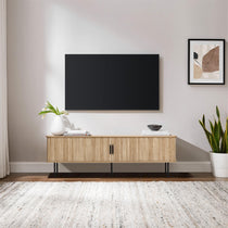 A minimalist living room showcases a 65-inch wall-mounted TV above an oak console with tambour doors, adorned with a vase and books. A framed abstract art piece and a potted plant rest elegantly on the light-colored rug.