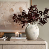 A multi-gray and white terracotta vase with handles from LuxenHome sits on a stone-textured table next to stacked books and a lit candle. The backdrop showcases an abstract art piece in neutral tones with marbled gray accents.