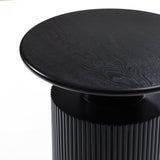 A close-up of a black circular side table highlights its textured wooden top, showcasing the natural wood grain, and a ribbed cylindrical base that exudes a modern aesthetic.