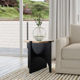 In a modern living room, the Bernard black and light wood finish side table by LuxenHome, made from manufactured wood, pairs with a round clear vase of greenery. It complements a cream sofa on a textured rug near large glass doors that open to reveal the outside deck and lush greenery.