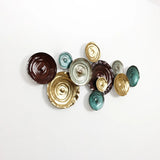 Wall art featuring an abstract design of textured, circular ceramic pieces in brown, gold, and teal hues, mounted against a white background.