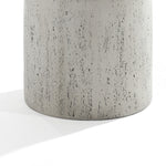 Close-up of the Rustic off White and Gray Outdoor Side Table by LuxenHome, 19.7 h. Crafted from concrete, its textured surface features small pits and grooves, casting a soft shadow against a white backdrop.