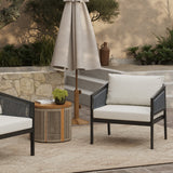 An outdoor armchair set featuring PE rattan design sits on the patio, accompanied by a small round table with a plant. Waterproof cushions provide comfort beneath the beige umbrella, while steps lead to lush greenery and a stone wall in the background.