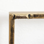 Close-up of a metal frame corner with visible welding marks and a textured, aged brass finish evokes an abstract metal wall decor piece against a plain white background.