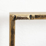 Close-up of a metal frame corner with visible welding marks and a textured, aged brass finish evokes an abstract metal wall decor piece against a plain white background.