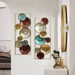 A hallway featuring two decorative wall sculptures with circular metallic designs in gold, teal, and brown tones, above a console table with modern art pieces, mirror, and a glimpse into a bedroom.