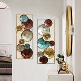 A hallway featuring two decorative wall sculptures with circular metallic designs in gold, teal, and brown tones, above a console table with modern art pieces, mirror, and a glimpse into a bedroom.