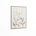 Framed artwork featuring two stylized branches with textured leaves and a subtle gold leaf motif on a neutral background, set against a plain white wall.