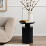 A modern side table with a black, ribbed base holds two books and a tall vase with branches. Its next to a beige sofa on a wooden floor showcasing its natural wood grain, with framed artwork partially visible on the wall, enhancing the modern aesthetic of the space.