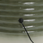 Close-up of a green, ribbed design surface with a black circular fixture and a cable extending from it, reminiscent of an LED water feature.