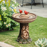 This charming polyresin garden birdbath, adorned with a face carved into the base, serves as a perfect outdoor decor centerpiece. Featuring two red bird figurines perched on top, its surrounded by vibrant flowers and lush greenery for a picturesque garden setting.