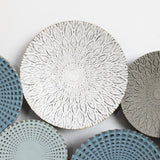 Decorative plates with intricate patterns add an artistic touch to your home decor; one central plate features a white floral design, surrounded by others in blue, grey, and green tones with textured patterns. Its like an abstract metal wall decoration for your walls.