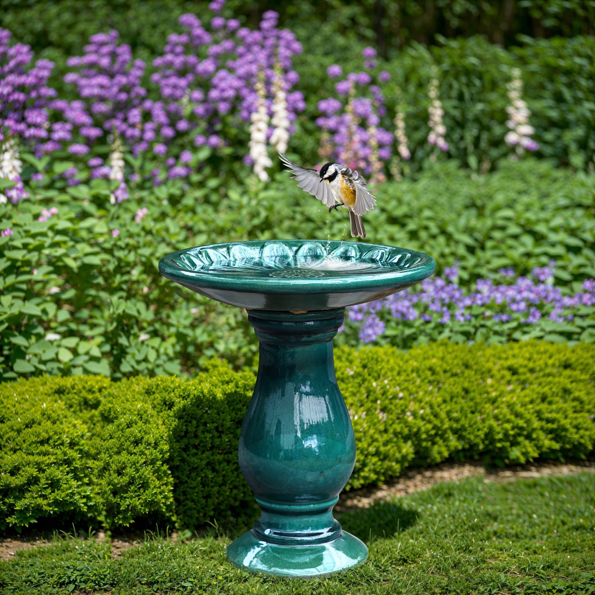 A bird with outstretched wings lands on a ceramic turquoise birdbath, nestled amidst green shrubs and purple flowers, enhancing the tranquility of the outdoor space.