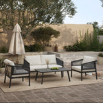 Outdoor conversation set featuring a PE rattan loveseat, two armchairs, and a coffee table on a rug. Black steel accents enhance the style, with a large umbrella and potted plants adding charm to the background.